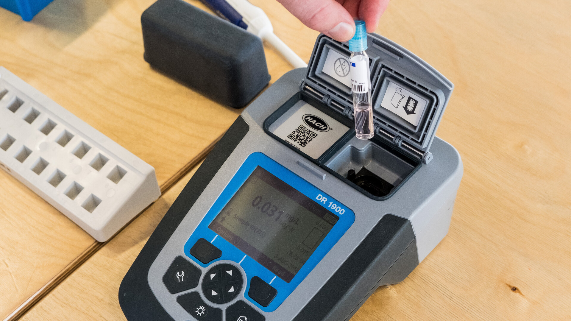 Eine Hand hält eine kleine Glasprobe über ein geöffnetes tragbares Messgerät (Photometer DR1900) zur Sedimentanalyse. Das Gerät zeigt einen Messwert auf dem Display an.