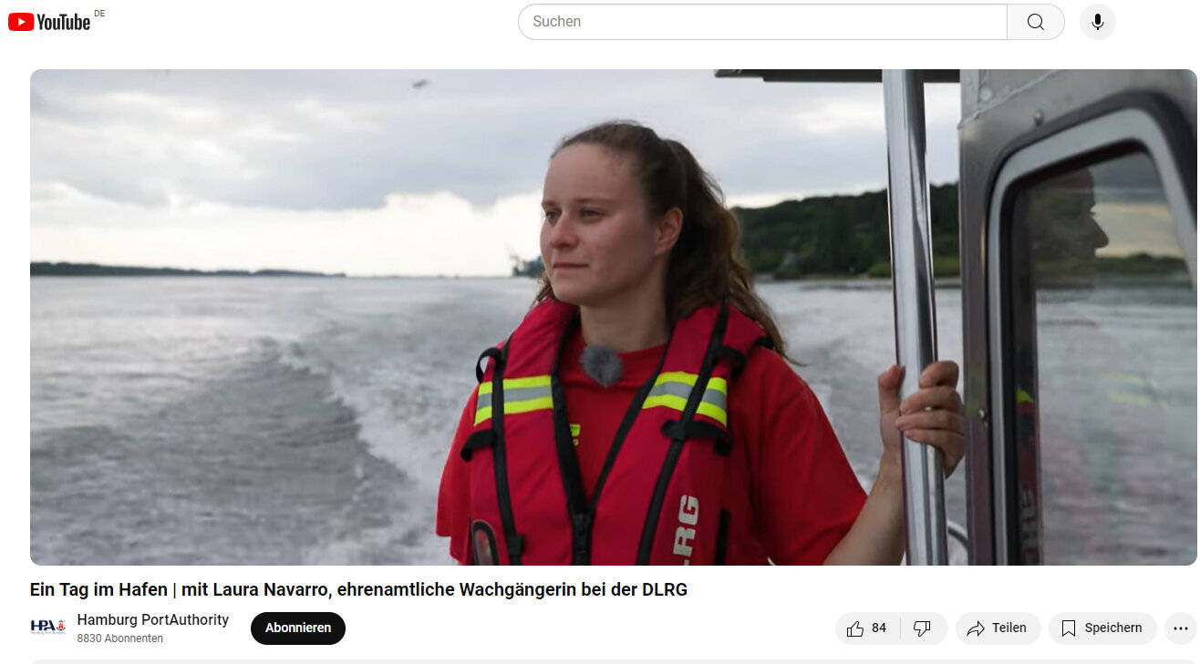 Laura Navarro vom DLRG steht mit Rettungsweste an Bord eines schnell fahrenden Schiffes und guckt auf die Elbe