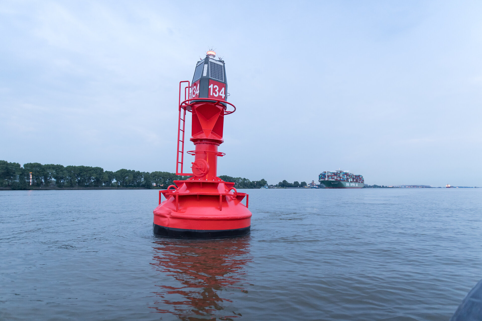 Rote Fahrwassertonne auf der Elbe mit einem Containerschiff im Hintergrund