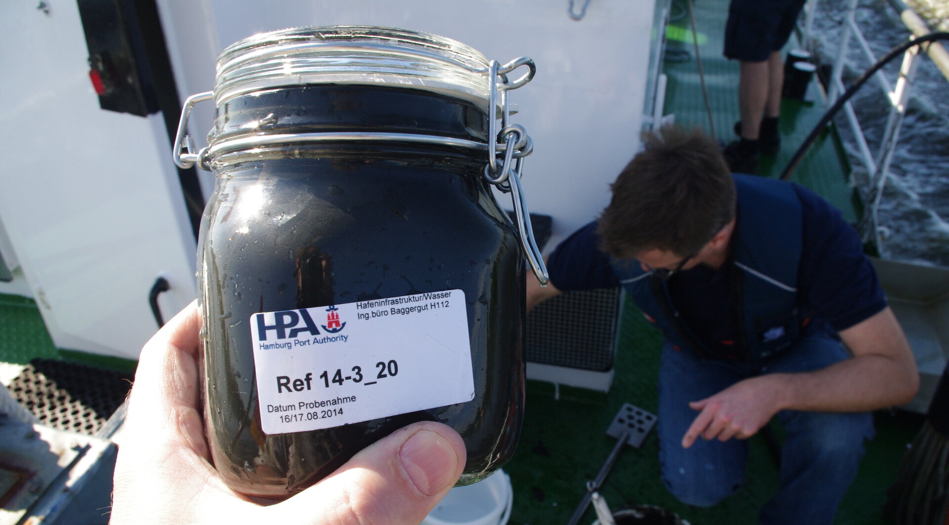 Auf dem Glas ist ein Etikett der Hamburg Port Authority (HPA) mit der Aufschrift „Ref 14-3_20“ sowie dem Probedatum „16/17.08.2014“ zu sehen