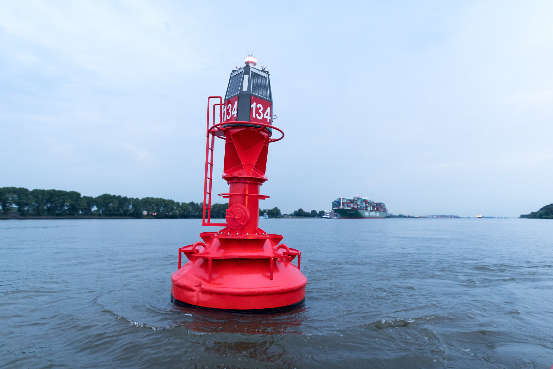 Rote Fahrwassertonne auf der Elbe mit einem Containerschiff im Hintergrund