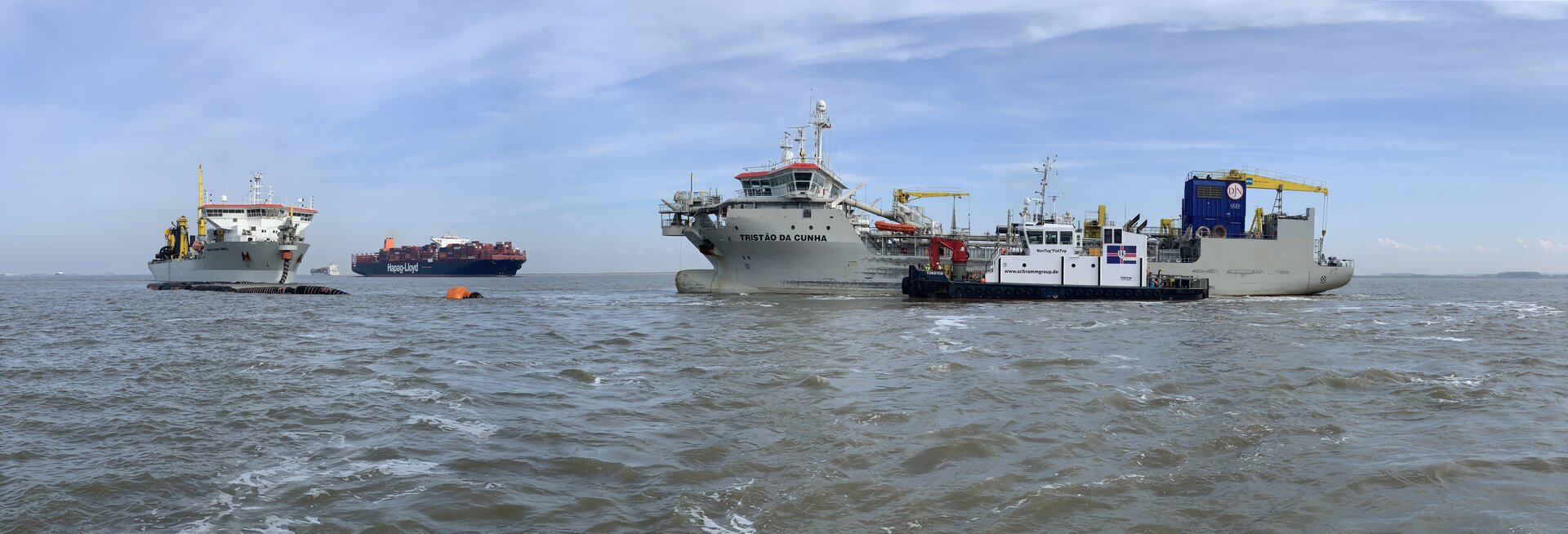Mehrere Baggerschiff auf der Elbe. Im Vordergrund das Baggerschiff „Tristão da Cunha“ mit angeschlossenem Arbeitsschiff, während ein weiteres Baggerschiff im Hintergrund arbeitet.